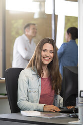 Porträt einer Geschäftsfrau am Schreibtisch mit kommunizierenden Kollegen im Hintergrund - FKF000544
