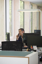 Porträt eines Geschäftsmannes beim Telefonieren am Arbeitsplatz - FKF000554