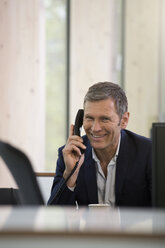 Portrait of smiling business man telephoning at workplace - FKF000555