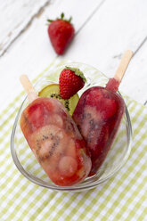 Glasschale mit zwei Kiwi-Erdbeer-Eislutschern, Erdbeere und Kiwi-Scheibe auf Stoff und Holz - SARF000652