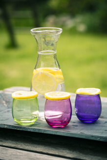 Wooden tray, carafe of lemonade and slices of lemon on coloured glasses - SARF000656