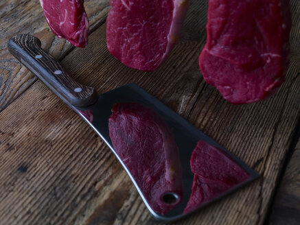 Pieces of raw beef lying on kitchen cleaver and wooden table - SRSF000496