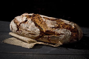 Crusty bread on jute in front of dark background - MAEF008329