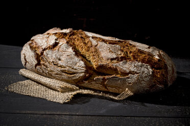 Krustiges Brot auf Jute vor dunklem Hintergrund - MAEF008329