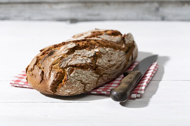 Krustiges Brot und Messer auf Stoff und weißem Holz - MAEF008332