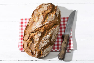 Krustiges Brot und Messer auf Stoff und weißem Holz - MAEF008333