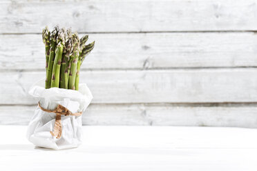 Bunch of green asparagus standing in white paper bag in front of white wood - MAEF008336