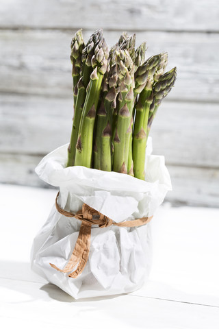 Bündel grüner Spargel in weißer Papiertüte vor weißem Holz stehend, lizenzfreies Stockfoto