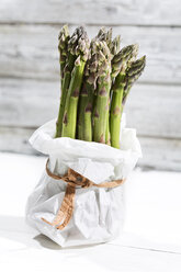 Bunch of green asparagus standing in white paper bag in front of white wood - MAEF008337