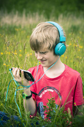 Porträt eines Jungen mit Smartphone und Kopfhörern auf einer Wiese - SARF000659