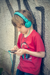 Porträt eines Jungen mit Smartphone und Kopfhörern vor einer Fassade - SARF000664