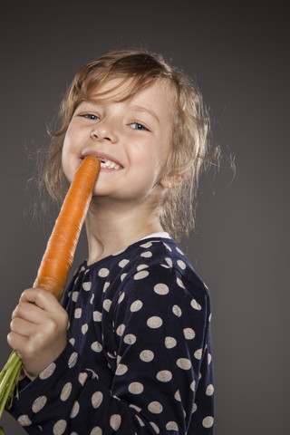 Porträt eines kleinen Mädchens, das eine Karotte als Mikrofon benutzt, lizenzfreies Stockfoto