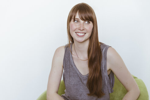 Portrait of smiling woman sitting on soft chair in front of white background - MFF001120