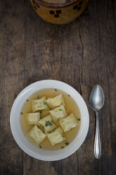 Soup dish of stock with Swabian dumplings and spoon on dark wood, elevated view - LVF001330