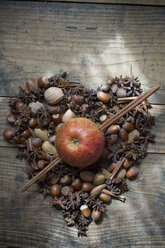 Herzform aus Sternanis, Nüssen und Zimtstangen mit Apfel durchbohrt aus Zimtstangen auf Holz - ASF005407