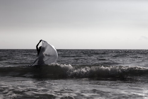 Silhouette einer jungen Frau, die mit einem Tuch am Meer spazieren geht - AJF000048