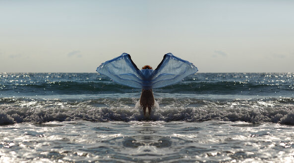 Silhouette einer jungen Frau vor dem Meer, die mit ausgestreckten Armen ein blaues Tuch hält - AJF000049