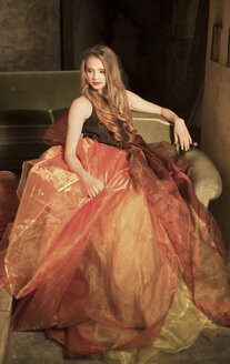 Portrait of young woman sitting at attic wearing orange skirt - FCF000226