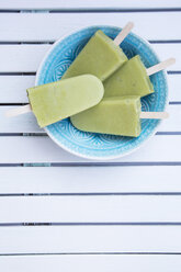 Bowl with four avocado ice lollies on white wood, elevated view - LVF001338