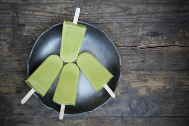 Bowl with four avocado ice lollies on dark wood, elevated view - LVF001339