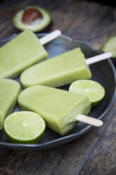 Bowl of avocado ice lollies and sliced limes - LVF001340