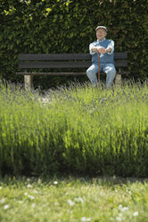 Happy old man sitting on park bench with lavender field in the foreground - UUF000679