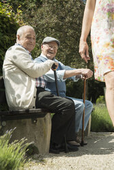 Two old men sitting on park bench watching legs of passing woman - UUF000740