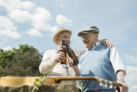 Zwei alte Freunde stoßen mit Bierflaschen im Park an, lizenzfreies Stockfoto