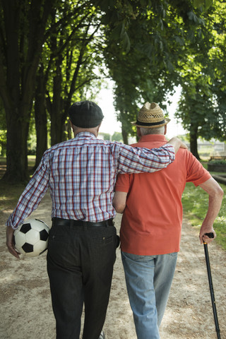 Zwei alte Freunde beim Spaziergang im Park mit Fußball, Rückansicht, lizenzfreies Stockfoto