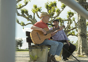 Deutschland, Rheinland-Pfalz, Worms, zwei alte Freunde mit Gitarre sitzen auf einer Bank an der Rheinuferpromenade - UUF000727