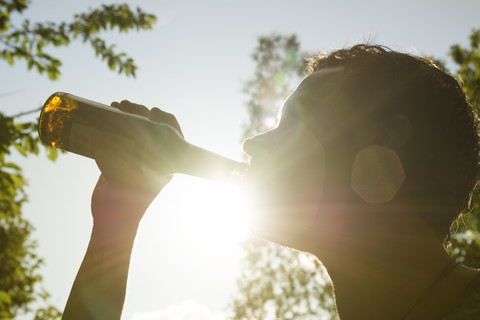 Mann trinkt Bier aus einer Flasche im Sonnenlicht, lizenzfreies Stockfoto