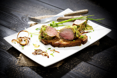 Schweinefilet auf knusprigem Brot mit Senf-Kräuterbutter und Rucola auf Teller - MAEF008370