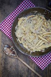 Holzlöffel und Bratpfanne mit fingerförmigen Kartoffelknödeln mit Sauerkraut und Speck auf Tuch - LVF001368