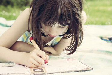 Porträt eines kleinen Mädchens, das auf einer Decke im Garten liegt und Tagebuch schreibt - LVF001361