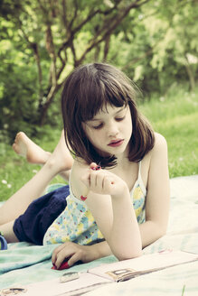 Portrait of little girl lying on blanket in the garden writing diary - LVF001362