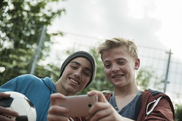 Two friends with soccer ball looking at cell phone - UUF000780