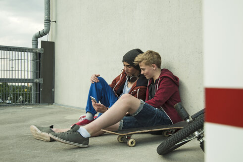 Zwei Jungen sitzen auf dem Boden und schauen auf ihr Handy - UUF000765