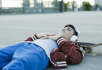 Boy wearing headphones lying on ground outdoors - UUF000809