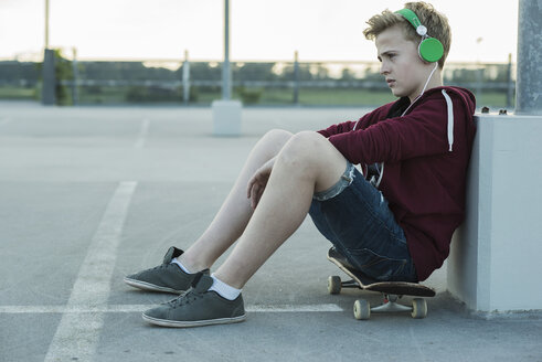 Seriöser Teenager auf einem Skateboard im Freien, der Musik hört - UUF000815