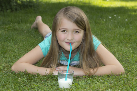 Mädchen liegt auf einer Wiese und trinkt Milch mit einem Trinkhalm, lizenzfreies Stockfoto