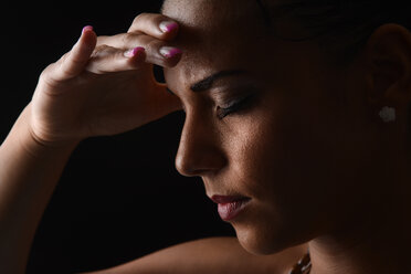 Porträt einer jungen Frau mit der Hand auf der Stirn vor einem schwarzen Hintergrund - BFRF000448