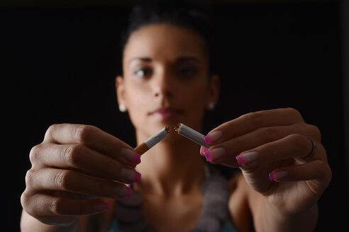 Junge Frau bricht eine Zigarette vor einem schwarzen Hintergrund - BFRF000452