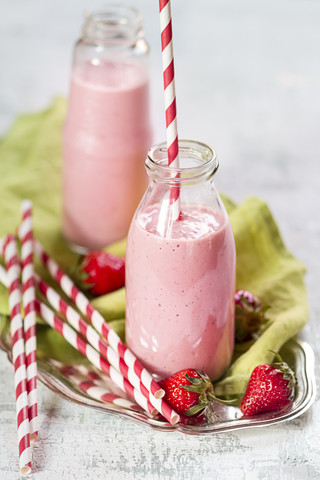 Zwei Flaschen Erdbeer-Rhabarber-Smoothie, Erdbeeren und Trinkstrawa auf einem Tablett, lizenzfreies Stockfoto