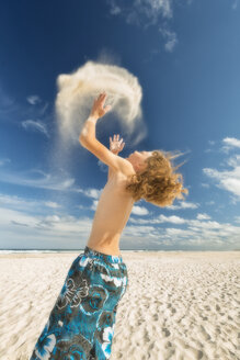 Australien, New South Wales, Pottsville, Junge am Strand wirft Sand in die Luft - SHF001345