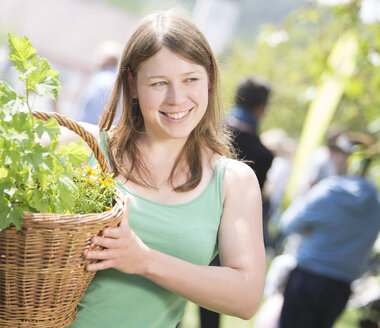 Porträt einer lächelnden jungen Frau, die einen Korb mit Pflanzen hält - DISF000839