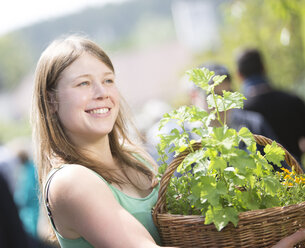 Porträt einer lächelnden jungen Frau, die einen Korb mit Pflanzen hält - DISF000840
