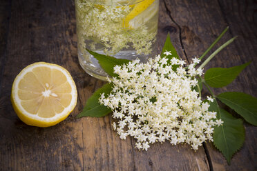 Glasflasche mit Holunderblütensirup, Holunderblüten und einer halben Zitrone auf dunklem Holz - LVF001382