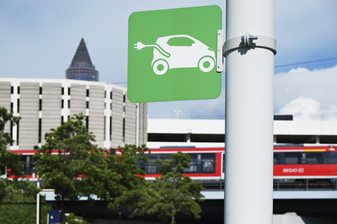 Schild für eine Ladestation für Elektrofahrzeuge mit einem Zug im Hintergrund, lizenzfreies Stockfoto