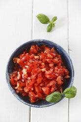 Bowl of diced tomatoes and basil leaves on white wood, elevated view - EVGF000627