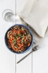 Bowl of spelt pasta with tomatoes and basil, glass of water, napkin and fork on white wood - EVGF000628